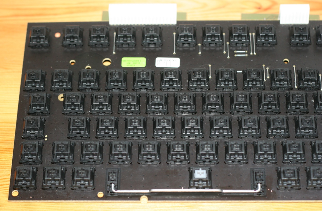 A picture of the clean and dry PCB, showing the left side with the switch for the spacebar (grey switch), after I tried to lubricate some of the switches. The shiny parts of the PCB (bottom left corner and the area near to the spacebar stabiliser) are the result of me smearing some of the silicon oil on the PCB by mistake and clumsiness...